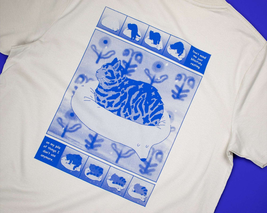 Bliss t-shirt | Hand screen printed on sand/beige organic cotton tee with blue comic style illustration of a tabby cat getting comfy