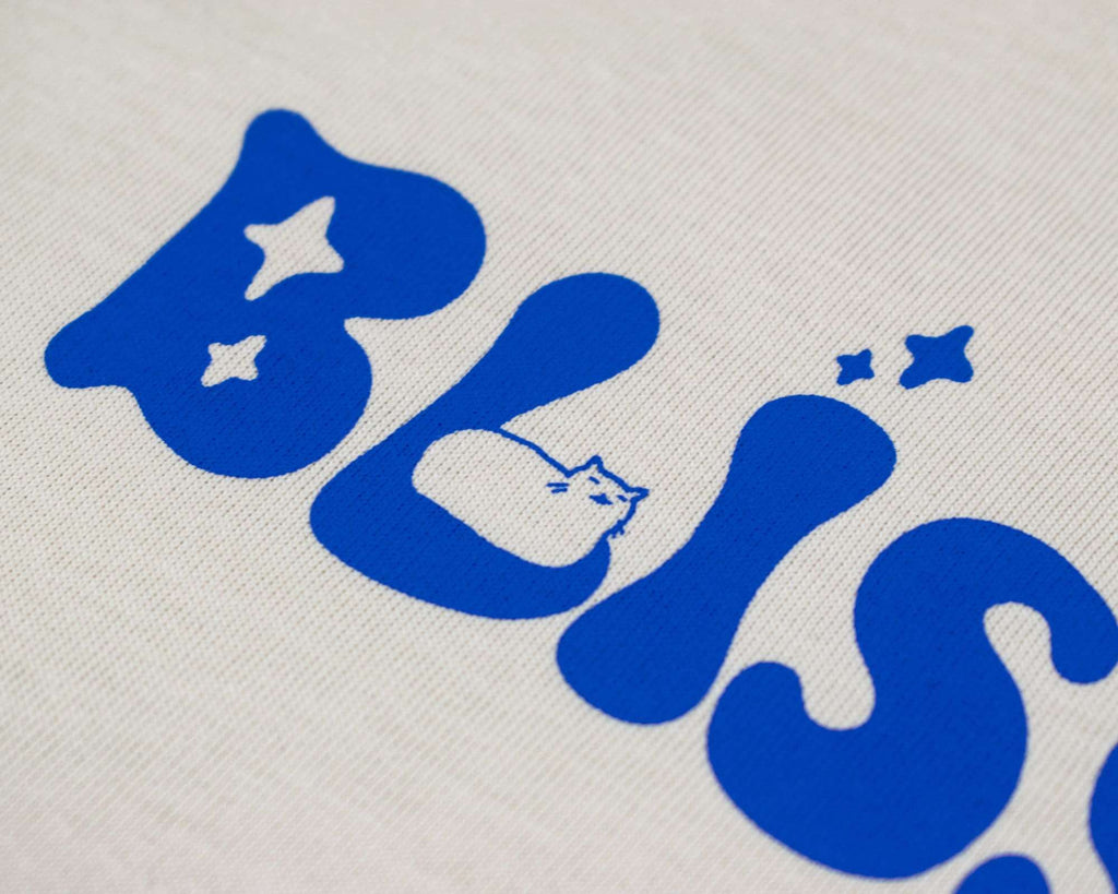 Bliss t-shirt | Hand screen printed on sand/beige organic cotton tee with blue comic style illustration of a tabby cat getting comfy