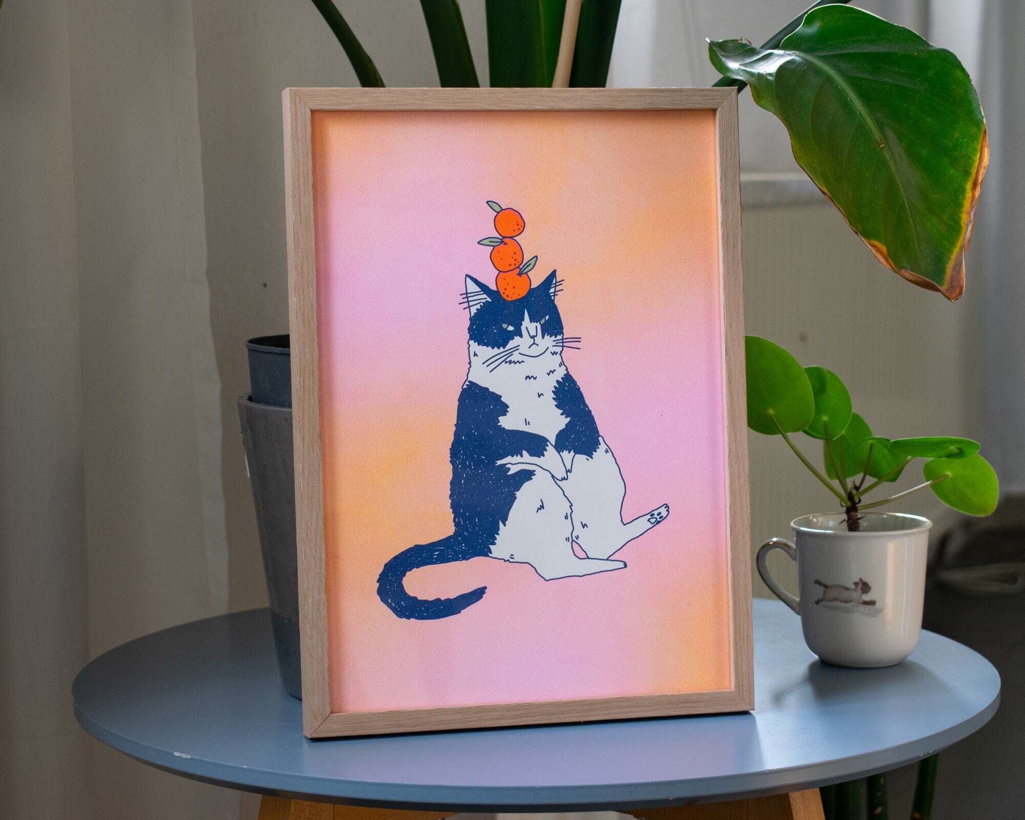 Orange Cat A4 Risograph poster | Illustration in fluorescent pink, yellow and federal blue of a grumpy cat that balances oranges on its head