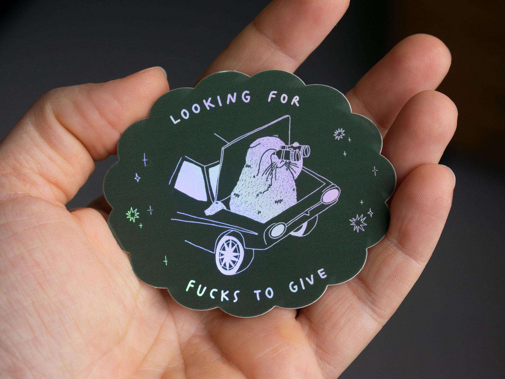 Looking for fucks to give 2.0 | Holographic Cat Sticker of a cat sitting in the trunk of a car looking for f***s to give through binoculars