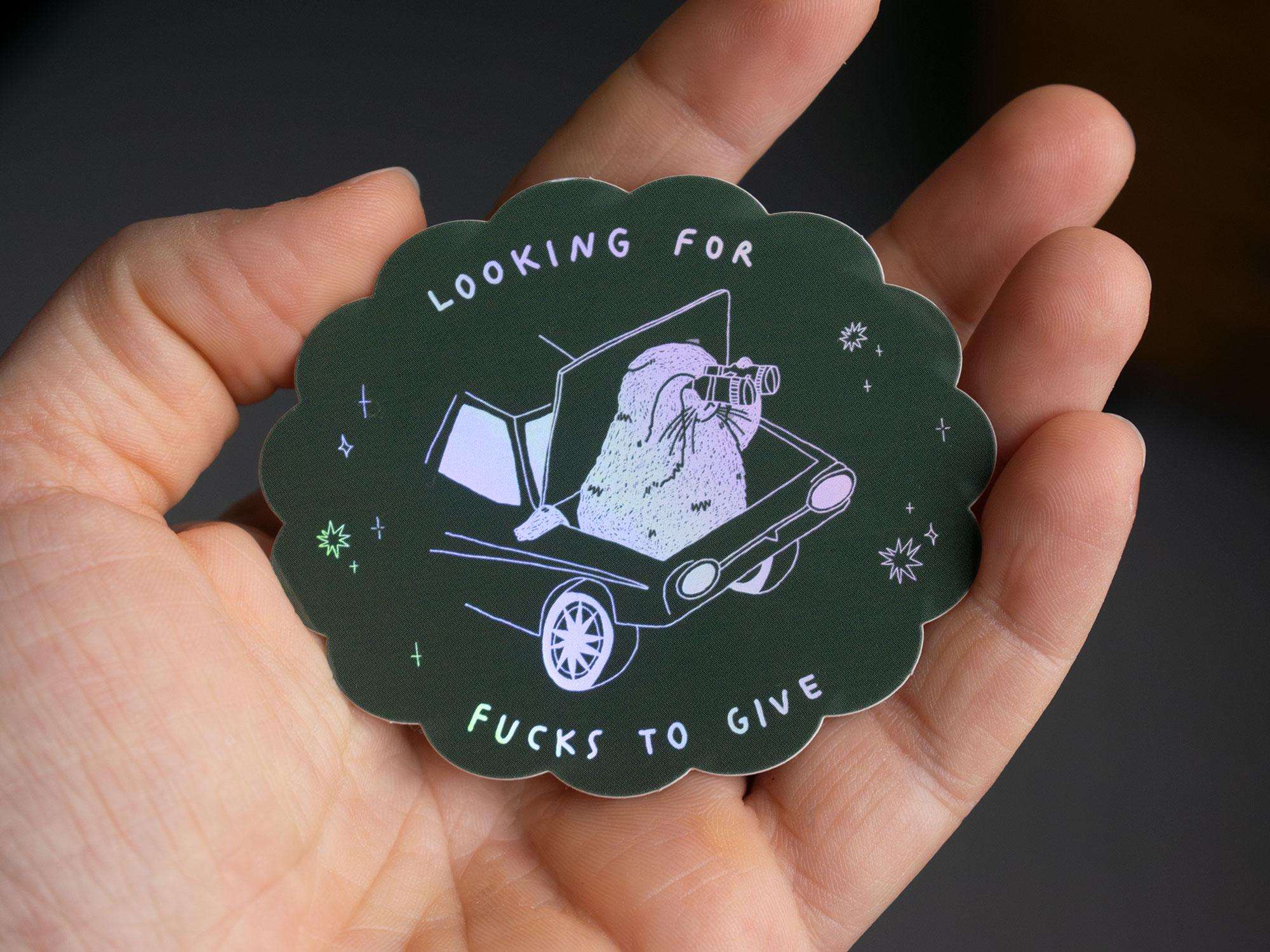 Looking for fucks to give 2.0 | Holographic Cat Sticker of a cat sitting in the trunk of a car looking for f***s to give through binoculars