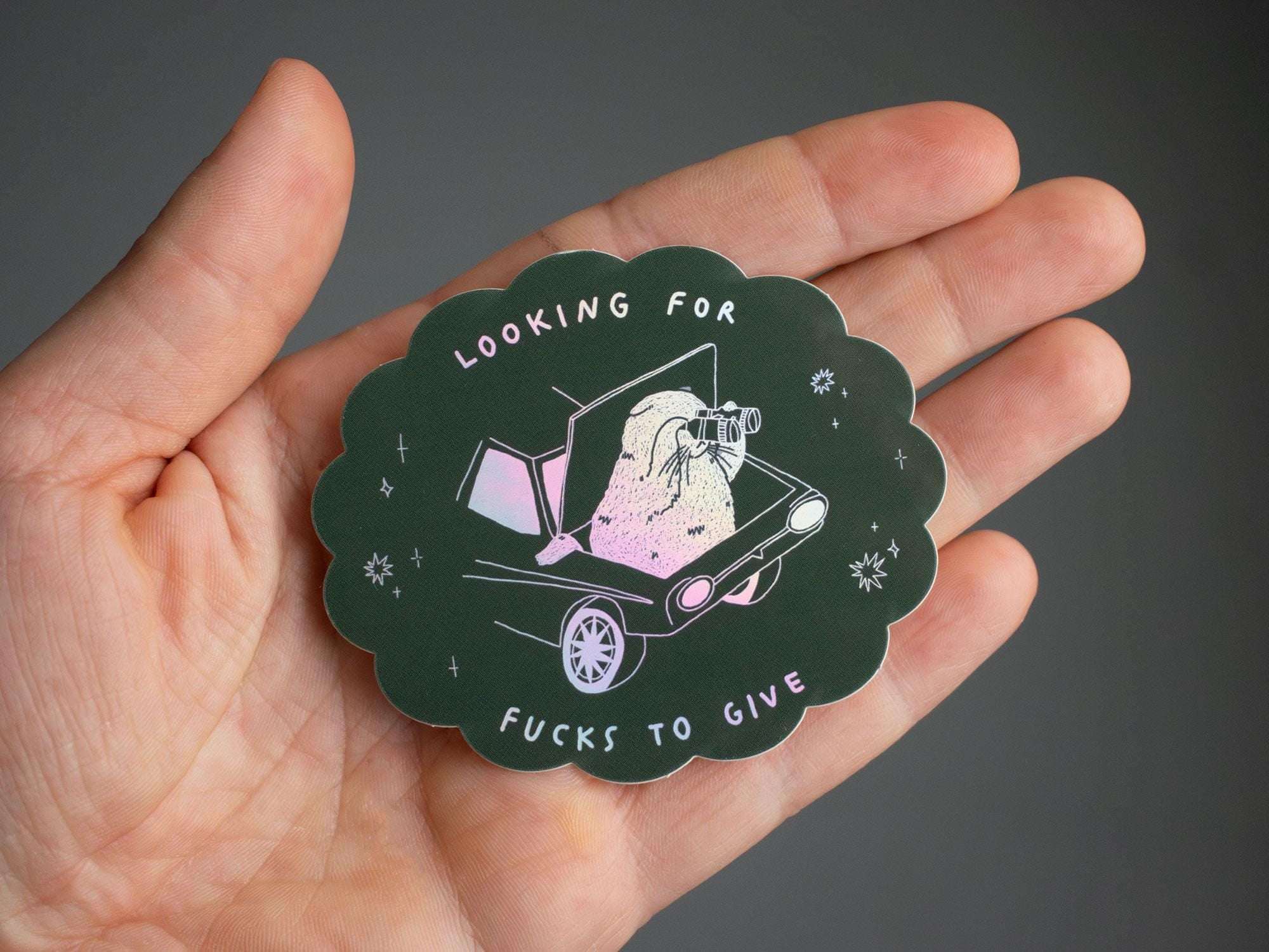 Looking for fucks to give 2.0 | Holographic Cat Sticker of a cat sitting in the trunk of a car looking for f***s to give through binoculars