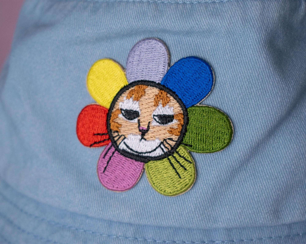 Grumpy Flower Bucket Hat | Sky blue fishermans hat with dtf printed or embroiderd patch of a grumpy cat with rainbow flower around is neck