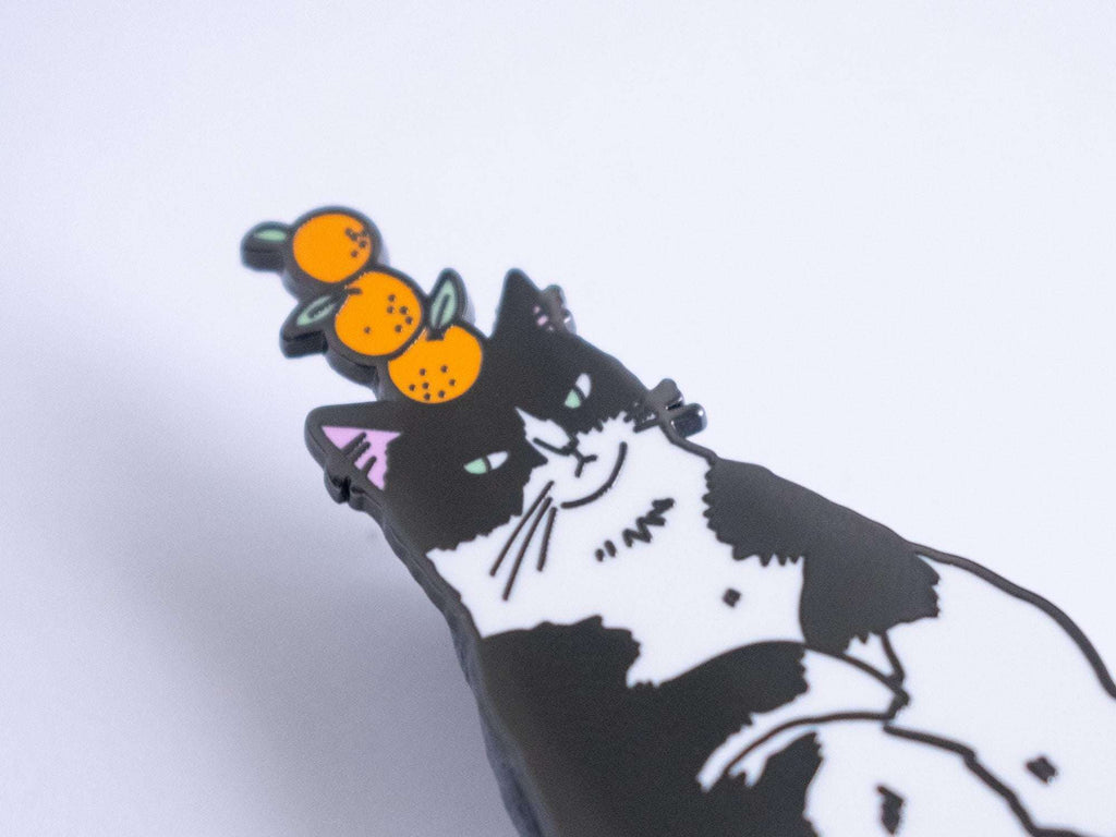 Orange Balance Cat Enamel Pin | Black nickel plated brooch with a tuxedo cat balancing three oranges on its head