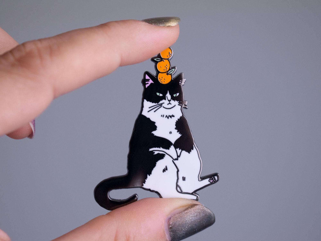 Orange Balance Cat Enamel Pin | Black nickel plated brooch with a tuxedo cat balancing three oranges on its head