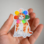 Grumpy Flower Cat | Holographic vinyl sticker of a irritable orange tabby cat wearing a rainbow colored flower petal costume around its head