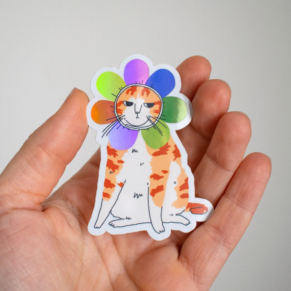 Grumpy Flower Cat | Holographic vinyl sticker of a irritable orange tabby cat wearing a rainbow colored flower petal costume around its head