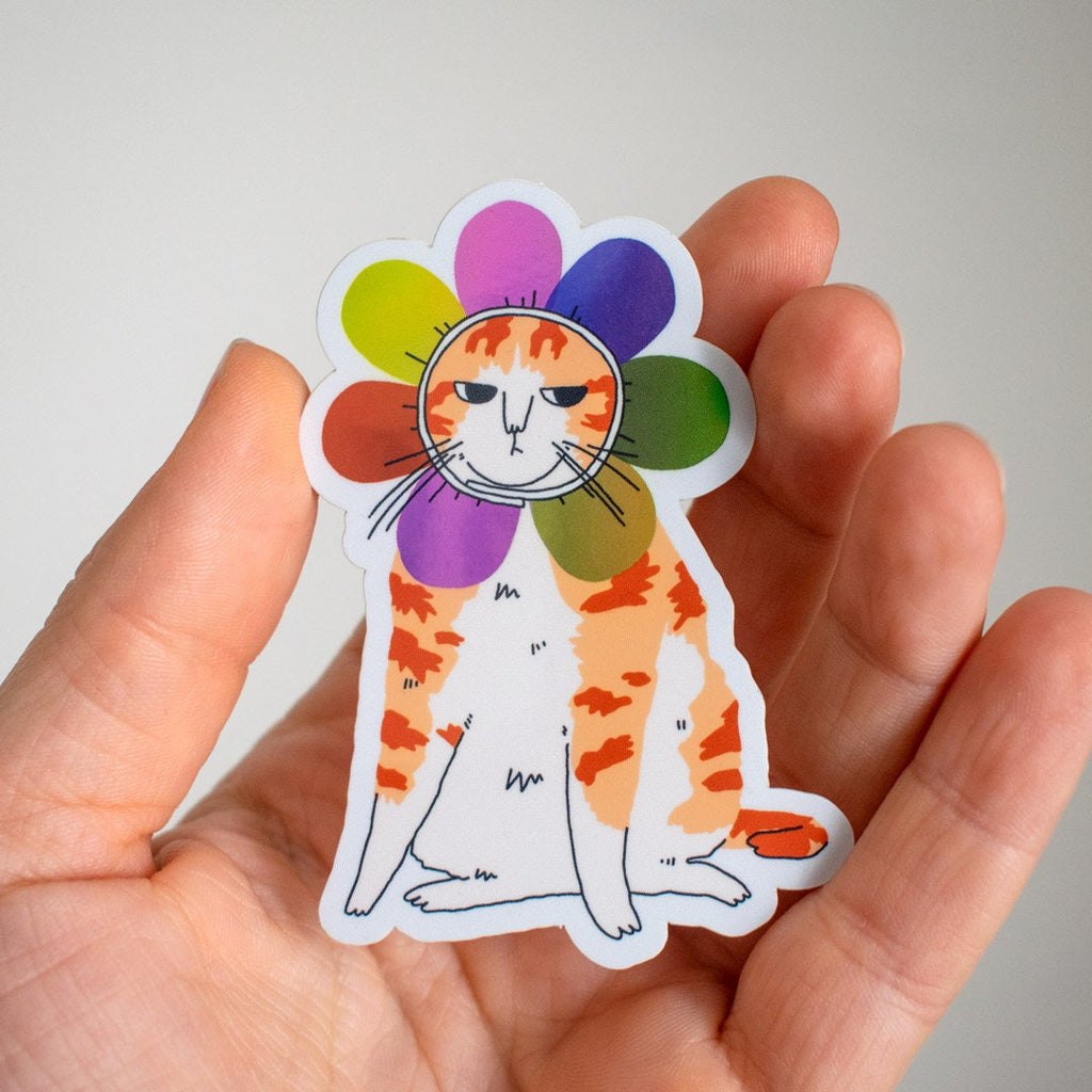 Grumpy Flower Cat | Holographic vinyl sticker of a irritable orange tabby cat wearing a rainbow colored flower petal costume around its head