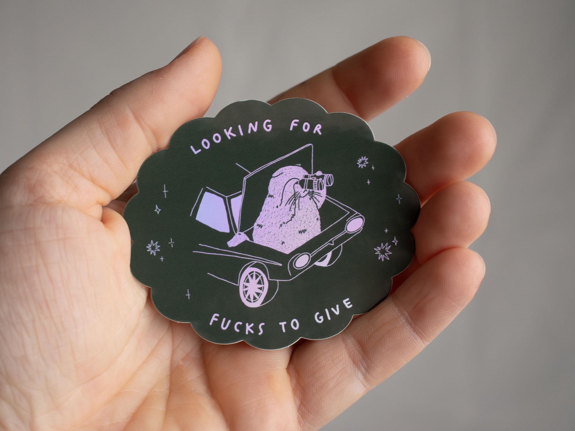 Looking for fucks to give 2.0 | Holographic Cat Sticker of a cat sitting in the trunk of a car looking for f***s to give through binoculars