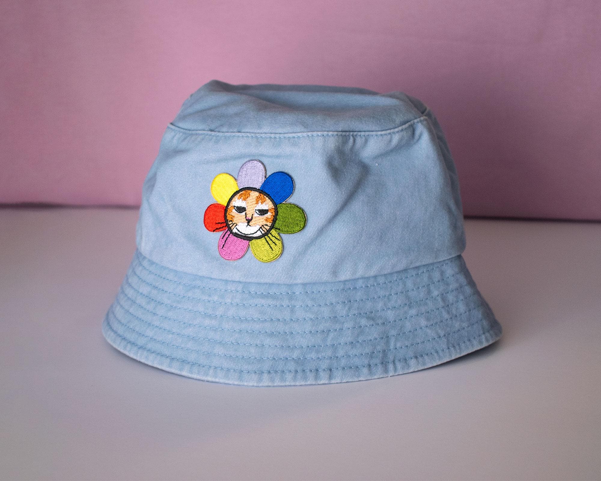 Grumpy Flower Bucket Hat | Sky blue fishermans hat with dtf printed or embroiderd patch of a grumpy cat with rainbow flower around is neck