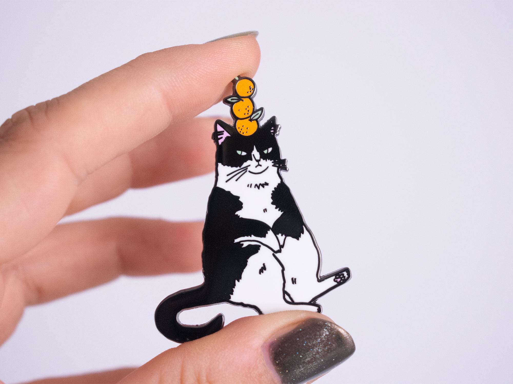 Orange Balance Cat Enamel Pin | Black nickel plated brooch with a tuxedo cat balancing three oranges on its head