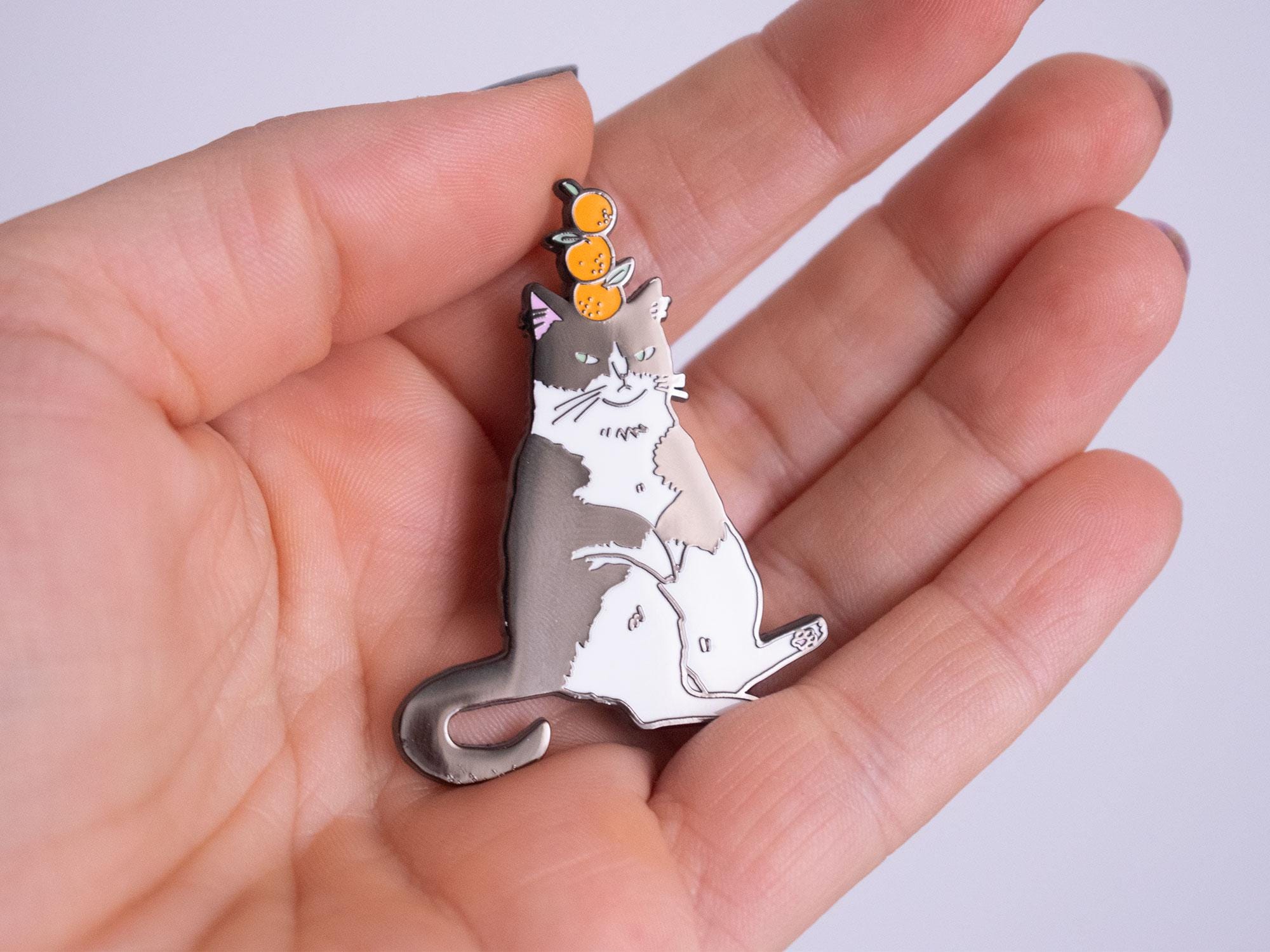 Orange Balance Cat Enamel Pin | Black nickel plated brooch with a tuxedo cat balancing three oranges on its head