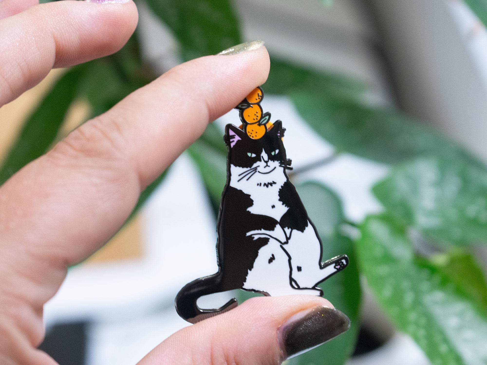 Orange Balance Cat Enamel Pin | Black nickel plated brooch with a tuxedo cat balancing three oranges on its head