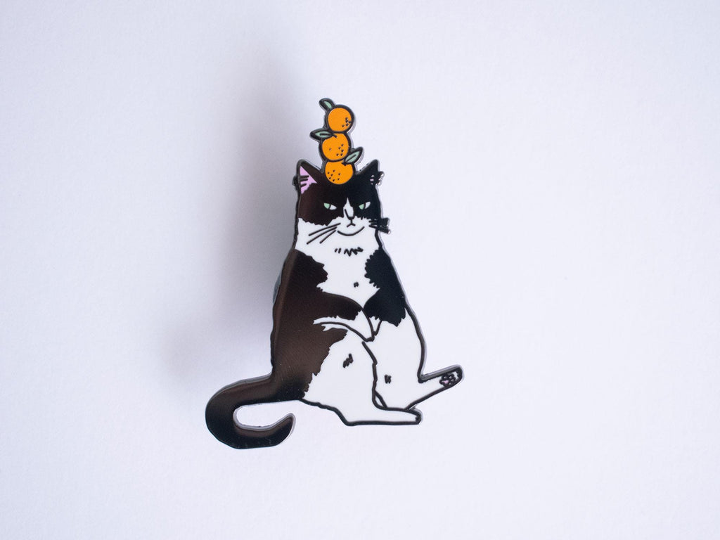Orange Balance Cat Enamel Pin | Black nickel plated brooch with a tuxedo cat balancing three oranges on its head