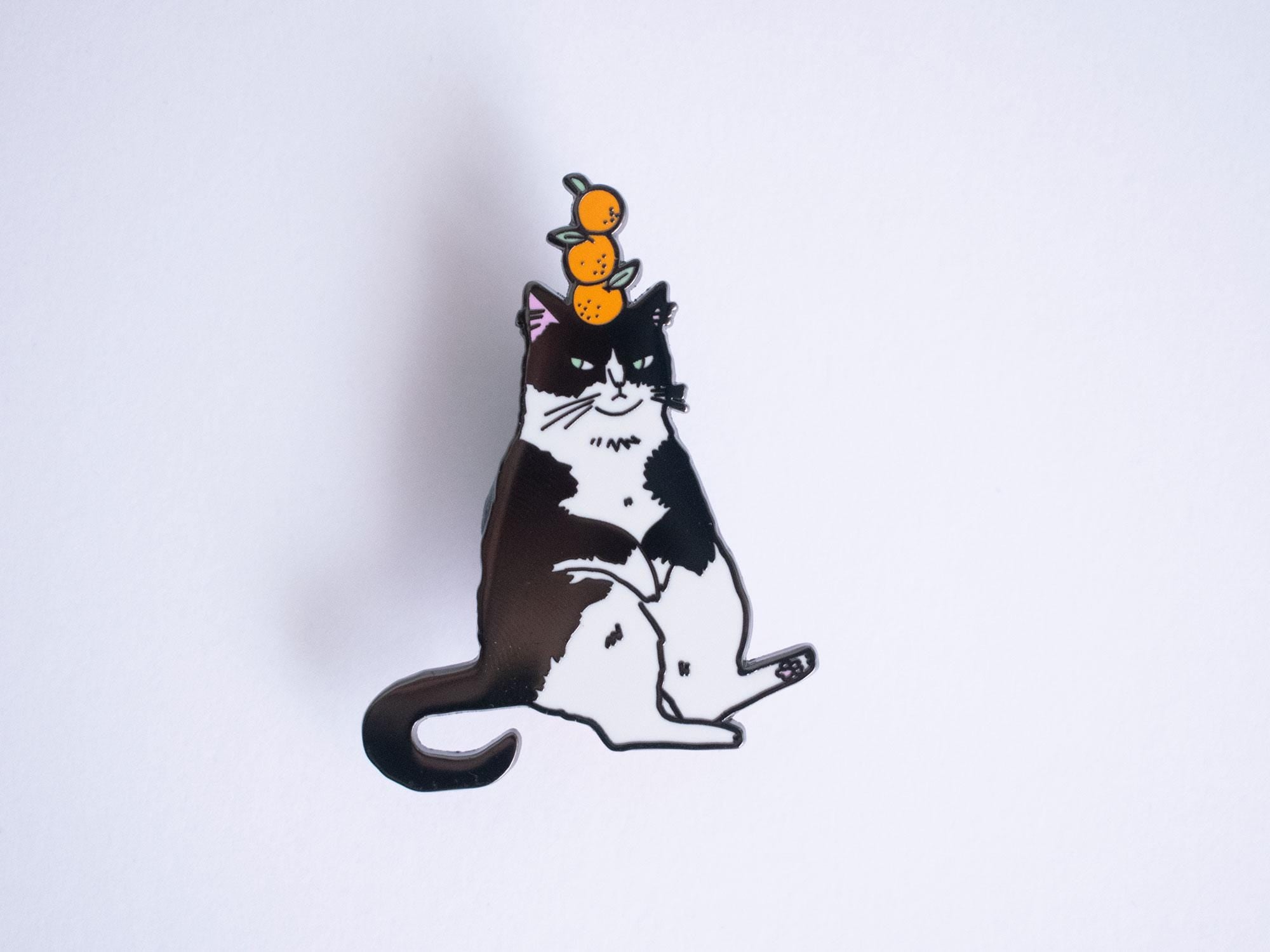 Orange Balance Cat Enamel Pin | Black nickel plated brooch with a tuxedo cat balancing three oranges on its head