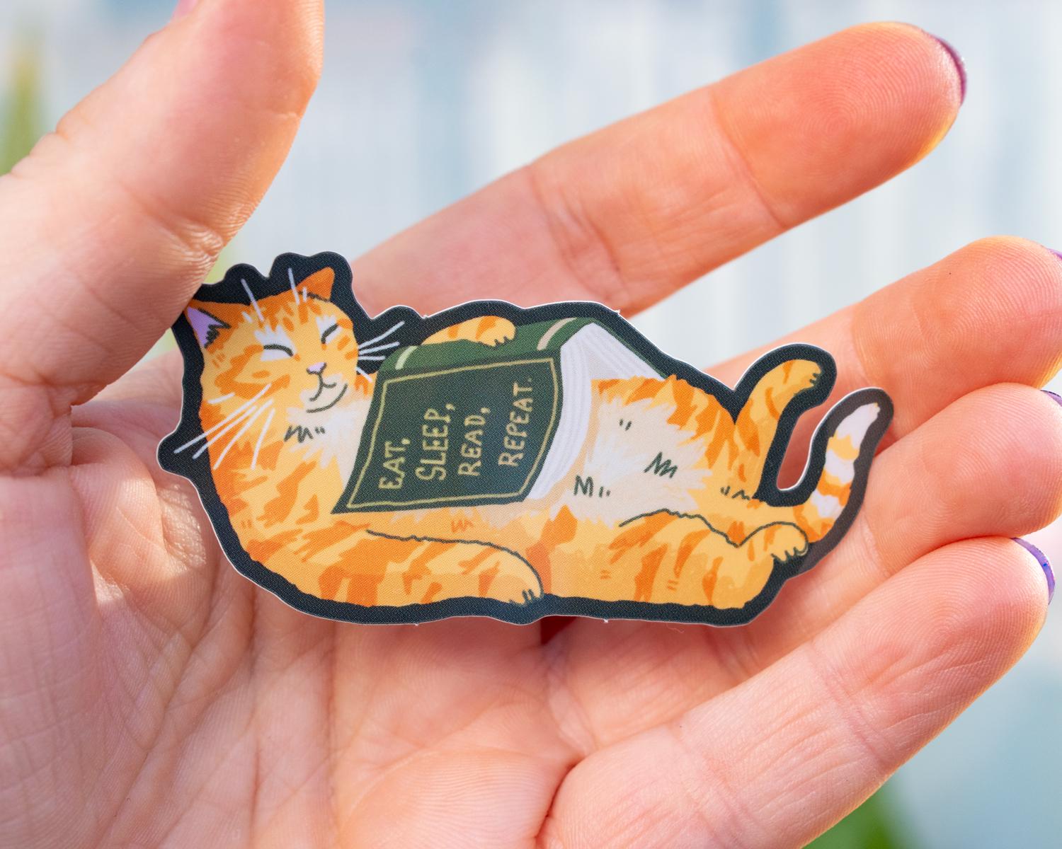 Eat, sleep, read, repeat | Holographic cat Sticker for bookish people with a sleepy orange cat and a green book in its belly