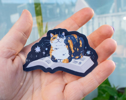 Read me | Holographic cat Sticker for bookish people with a calico cat sitting on a book