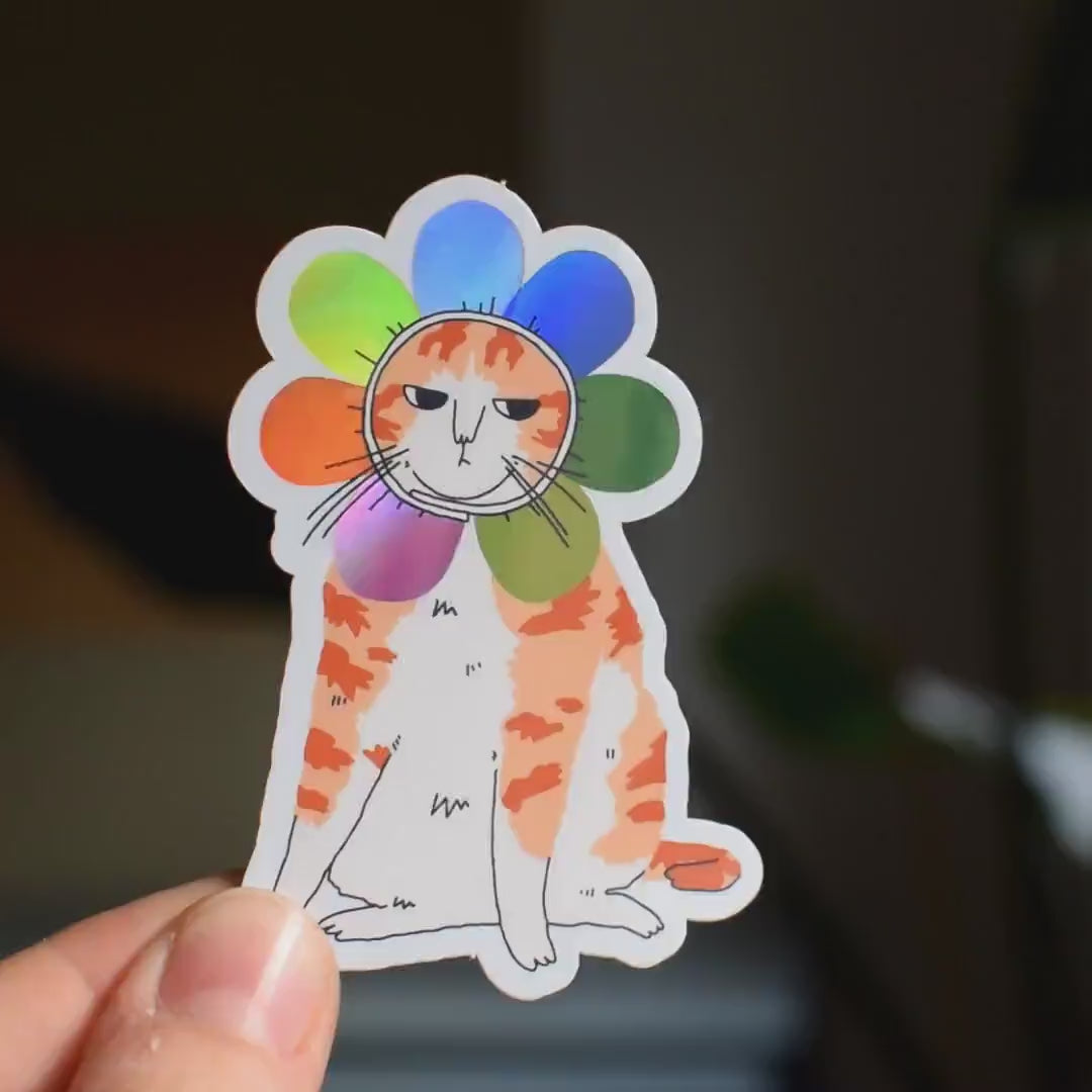 Grumpy Flower Cat | Holographic vinyl sticker of a irritable orange tabby cat wearing a rainbow colored flower petal costume around its head